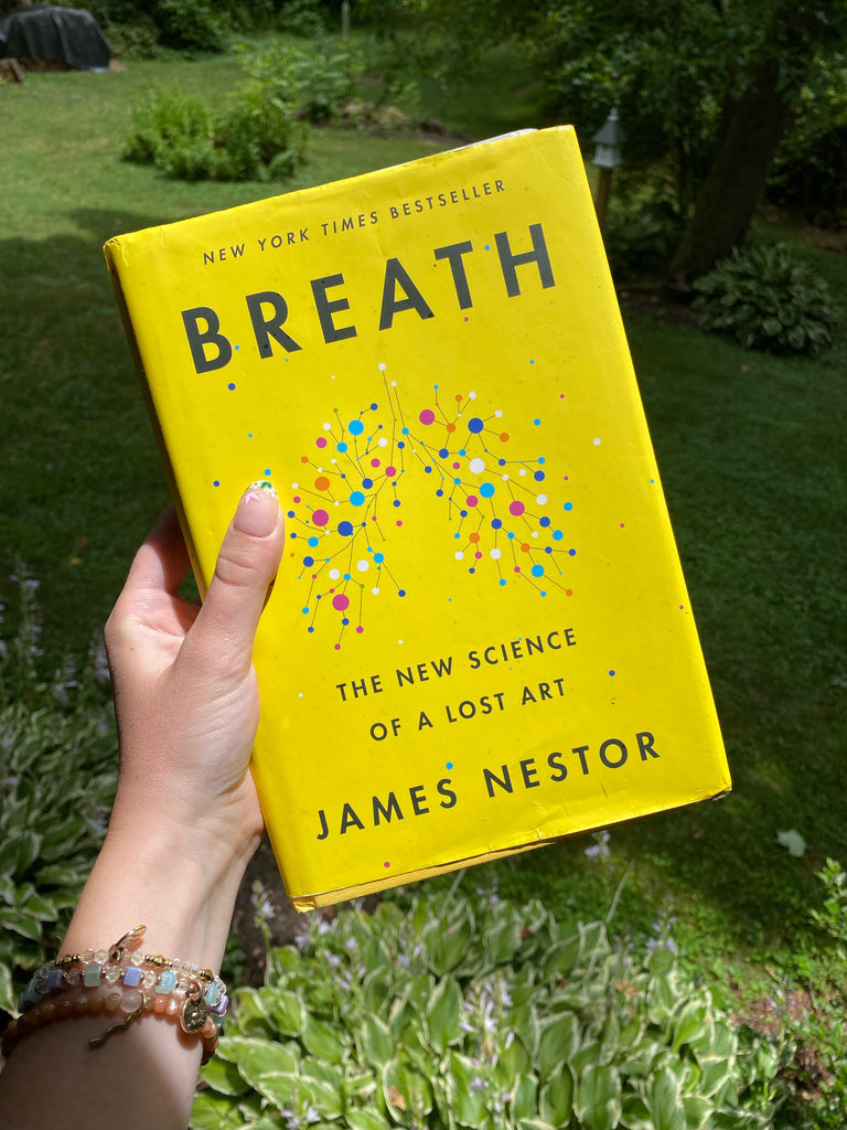hand holding book "Breath" by James Nestor over outdoor greenery background